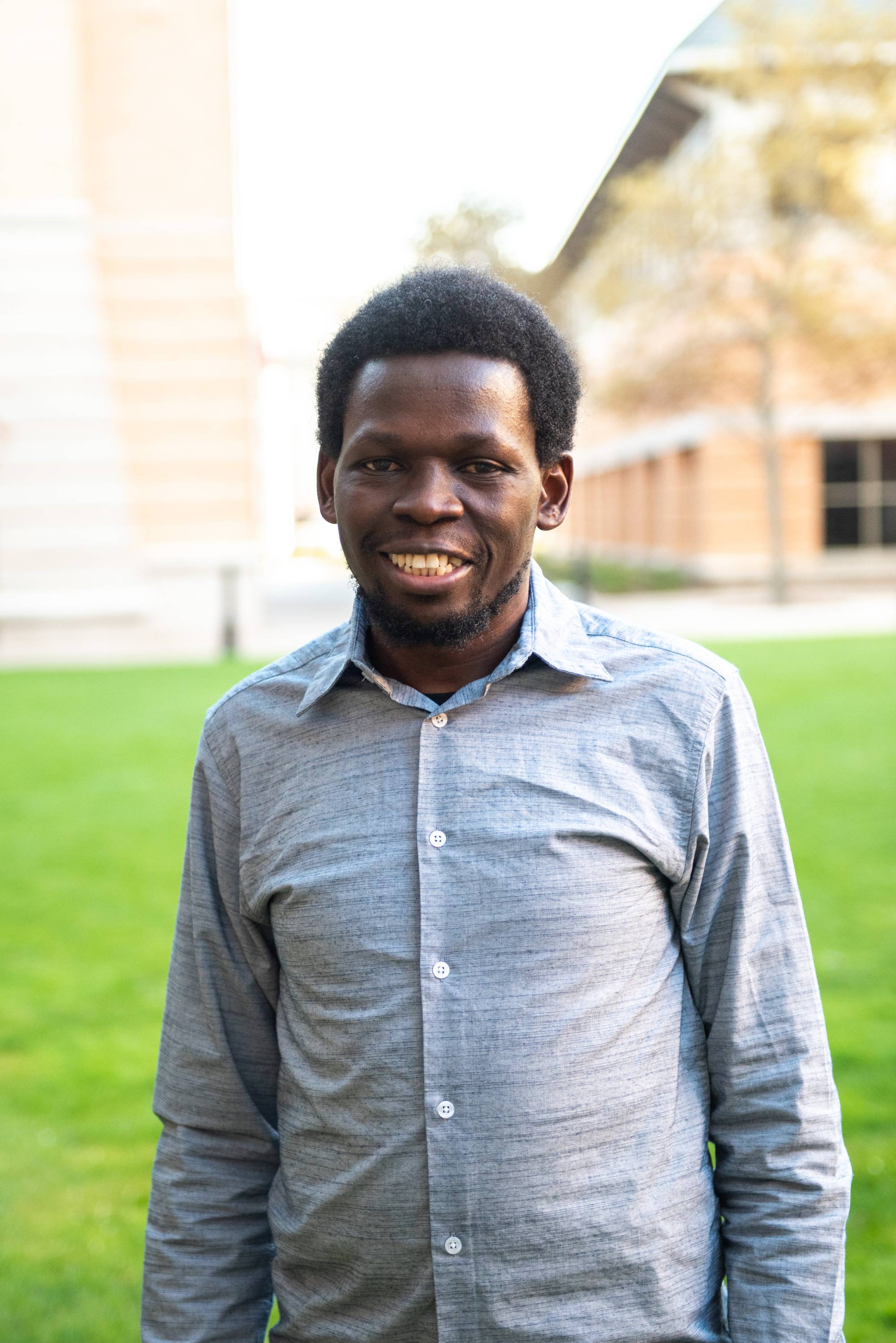 Student wearing light blue button up shirt smiling at the camera with brick building in the background